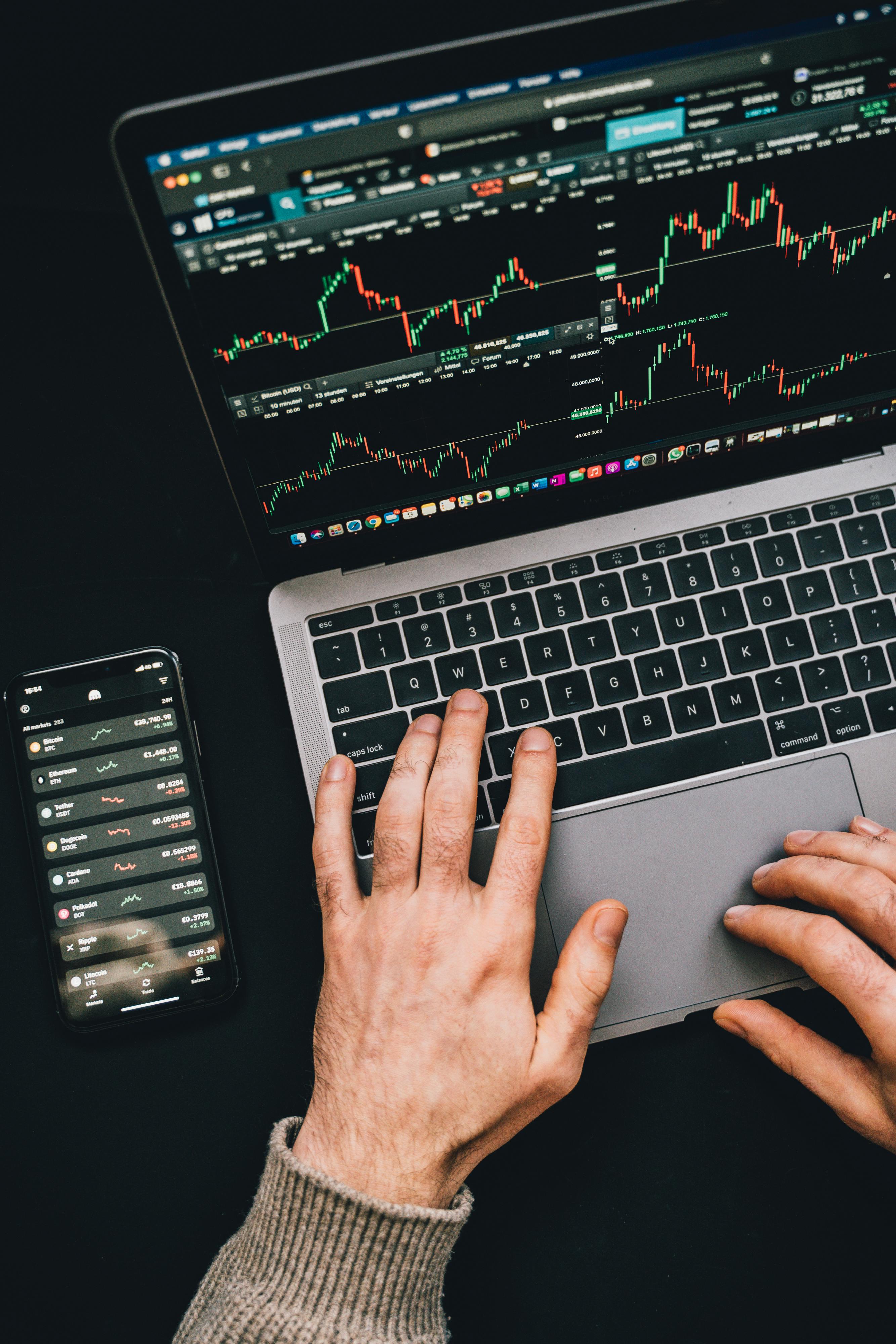 Hands using a laptop and phone to trade on CM Capital