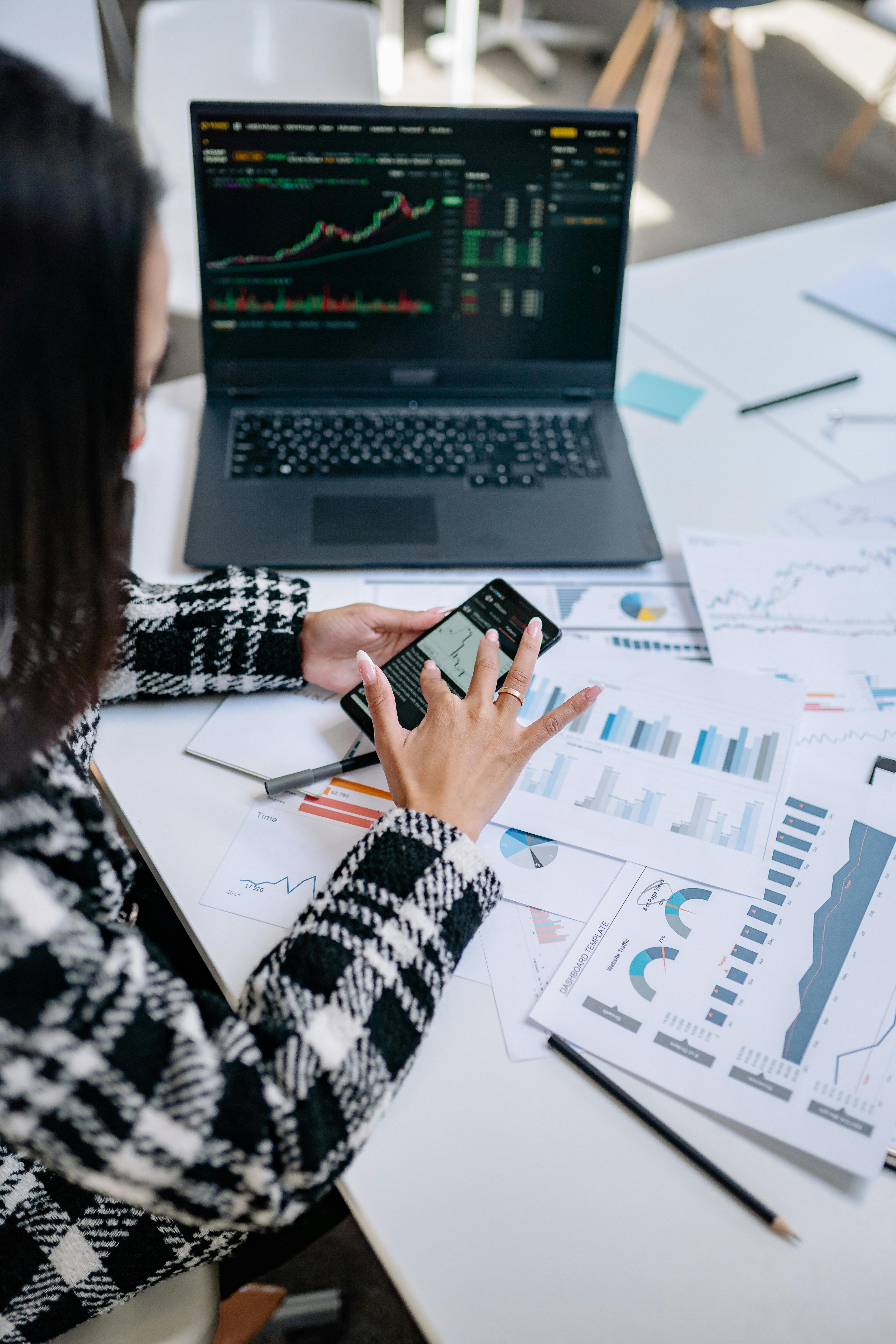 Woman analyzing stock charts on a laptop and smartphone
